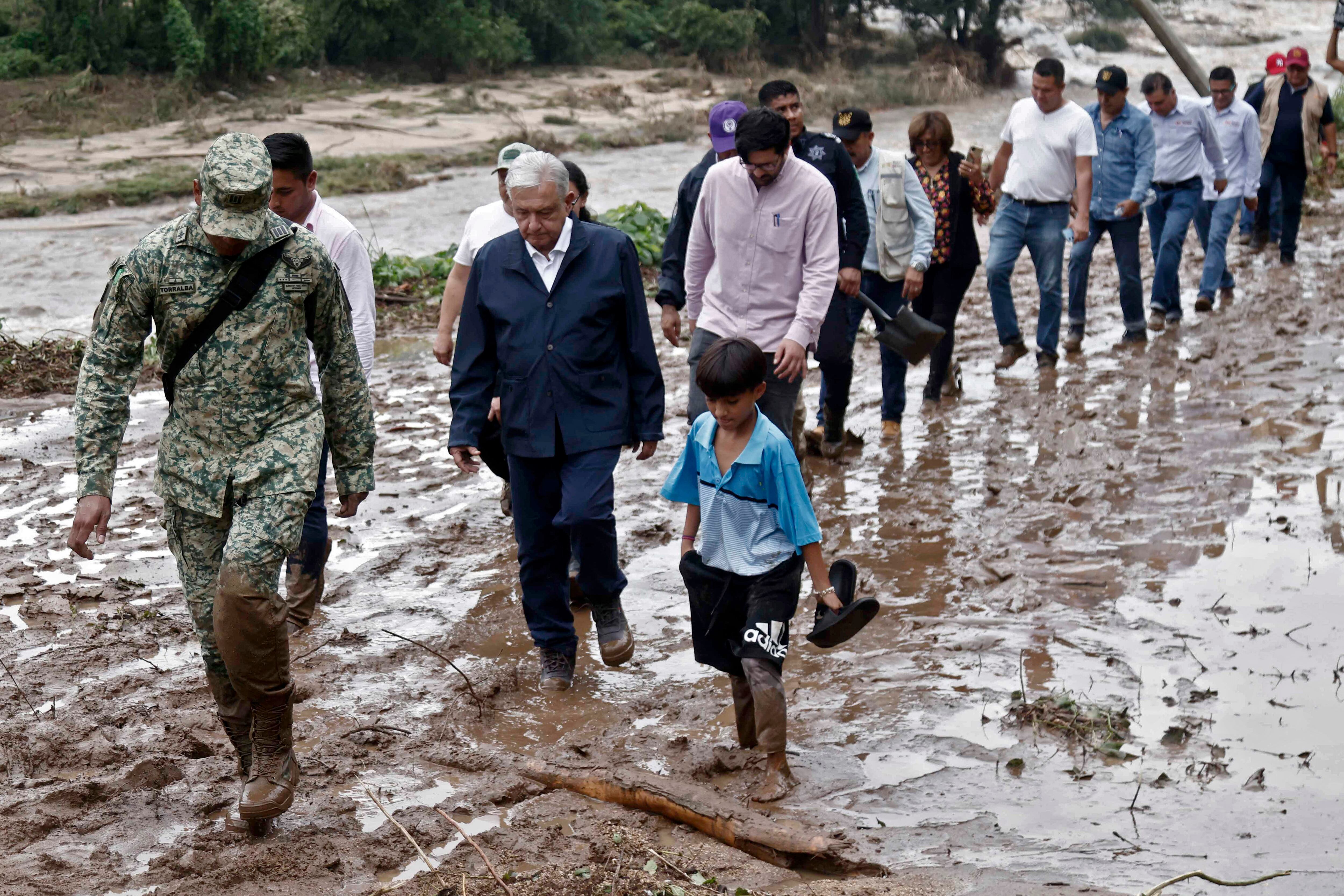 El presidente mexicano, Andrés Manuel López Obrador, y miembros de su gabinete caminan sobre el barro mientras visitan la comunidad El Kilometro 42, cerca de Acapulco. (Foto de RODRIGO OROPEZA/AFP).
