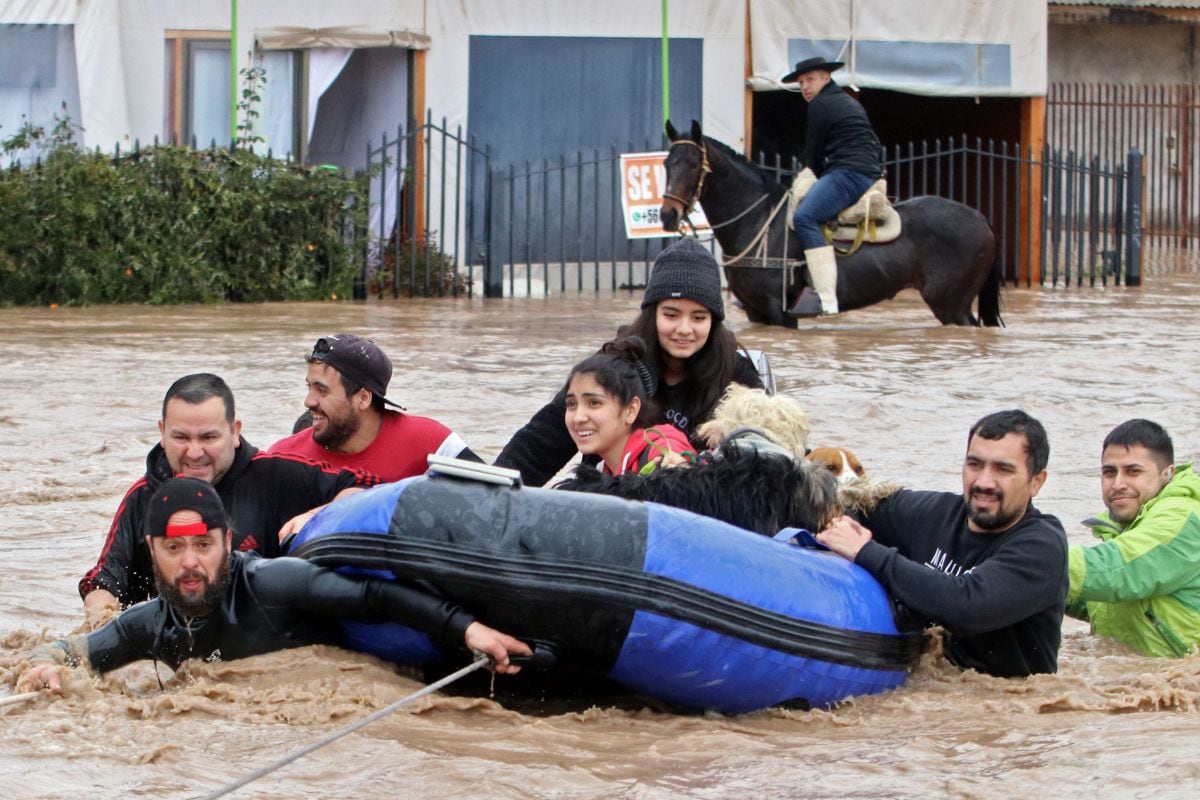 Personas y perros rescatados en un bote inflable en Coltauco, Rancagua, al sur de Santiago, el 24 de junio de 2023, luego de que las fuertes lluvias en la región provocaron el desbordamiento del río Cachapoal (Foto: Jorge Loyola / ATON CHILE / AFP)