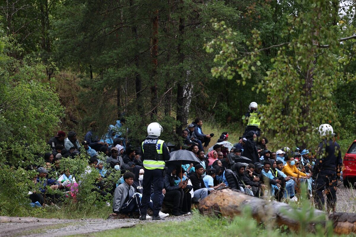 Gente se sienta en el suelo junto a los policías después de los enfrentamientos en el festival cultural eritreo "Eritrea Scandinavia" en Järvafältet, en el norte de Estocolmo, el 3 de agosto de 2023. (Foto de ALI LORESTANI / TT News Agency / AFP)