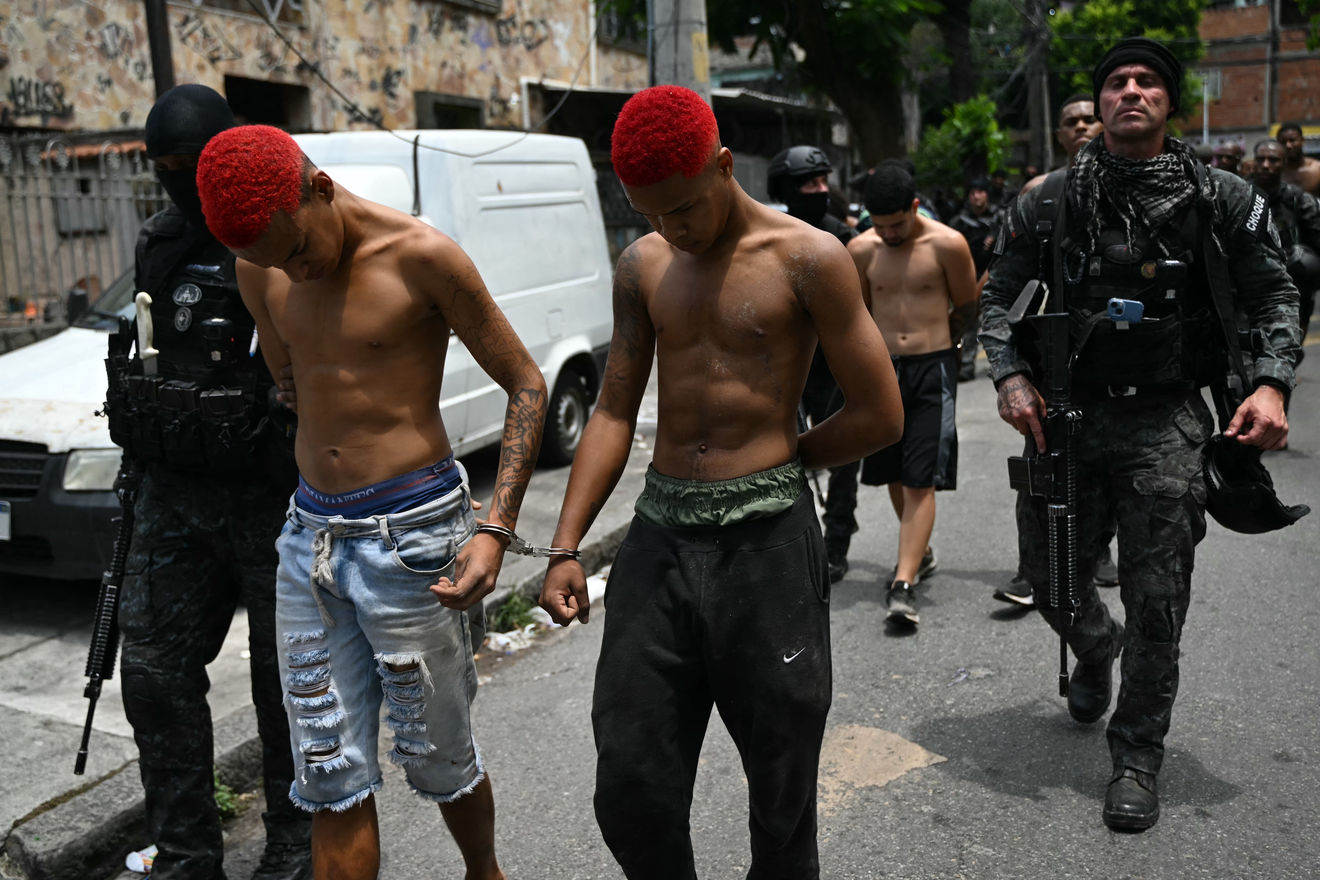 Agentes de policía escoltan a sospechosos arrestados durante la Operación Contención en el complejo Penha, Río de Janeiro. (Foto de Mauro PIMENTEL / AFP).