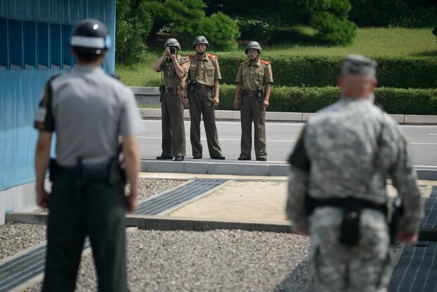 Soldados norcoreanos (C) toman fotos hacia un soldado surcoreano (L) y un soldado estadounidense (R) de pie ante la línea de demarcación militar (C inferior) que separa Corea del Norte y Corea del Sur dentro de la Zona de Seguridad Conjunta (JSA) en Panmunjom el 27 de julio de 2014. (Foto: AFP)