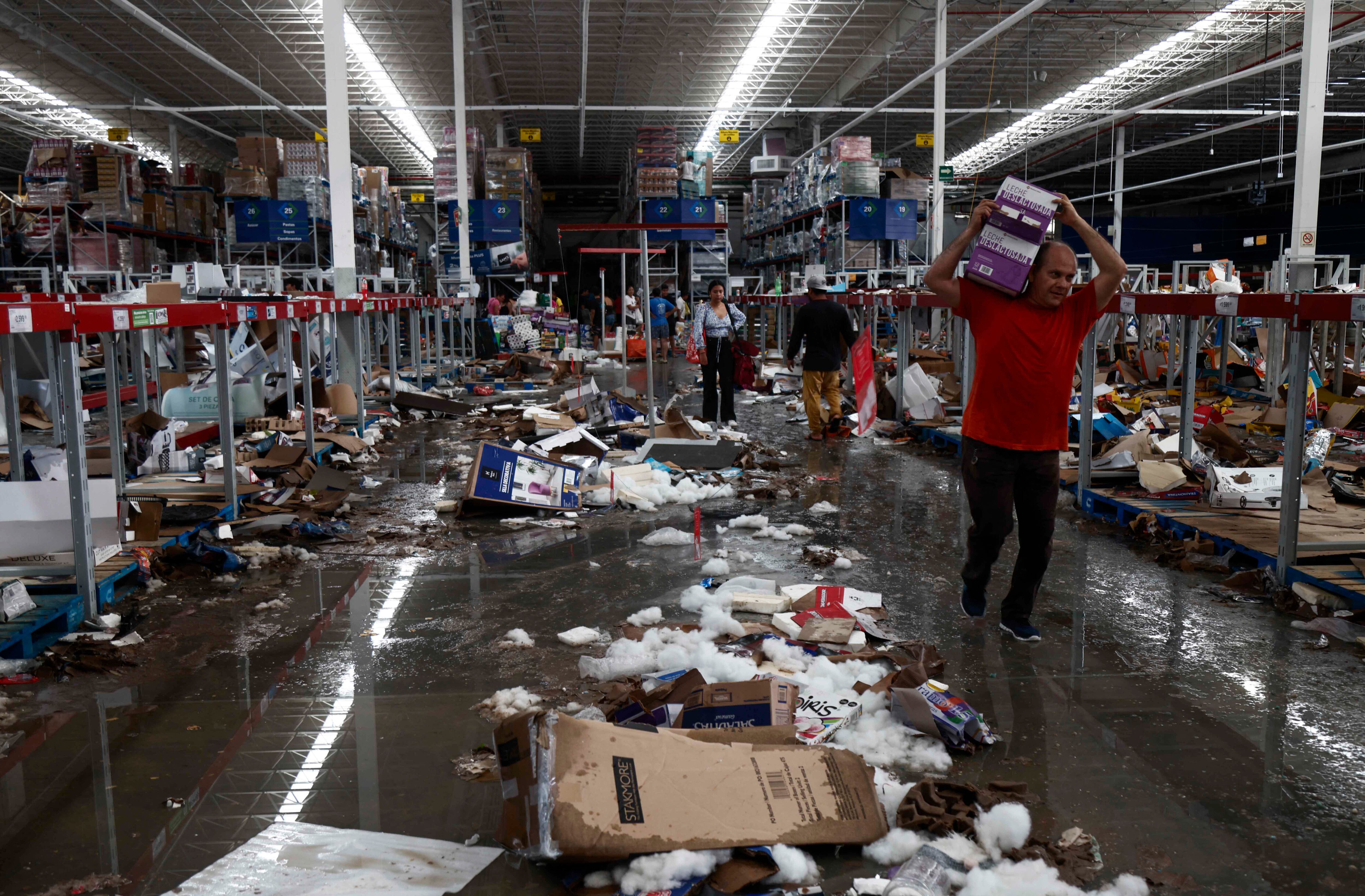 La gente recoge comestibles en un supermercado saqueado después del paso del huracán Otis en Acapulco, estado de Guerrero, México, el 26 de octubre de 2023. (Foto de RODRIGO OROPEZA/AFP).