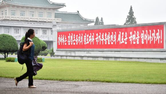 Una mujer pasa junto a una pancarta roja que se traduce como "¡Abramos la nueva fase de prosperidad y desarrollo nacional siguiendo el liderazgo del respetado camarada Kim Jong Un!", exhibida a lo largo de la calle Pothongmun en Pyongyang el 11 de agosto de 2023 | Foto: Kim Won Jin / AFP