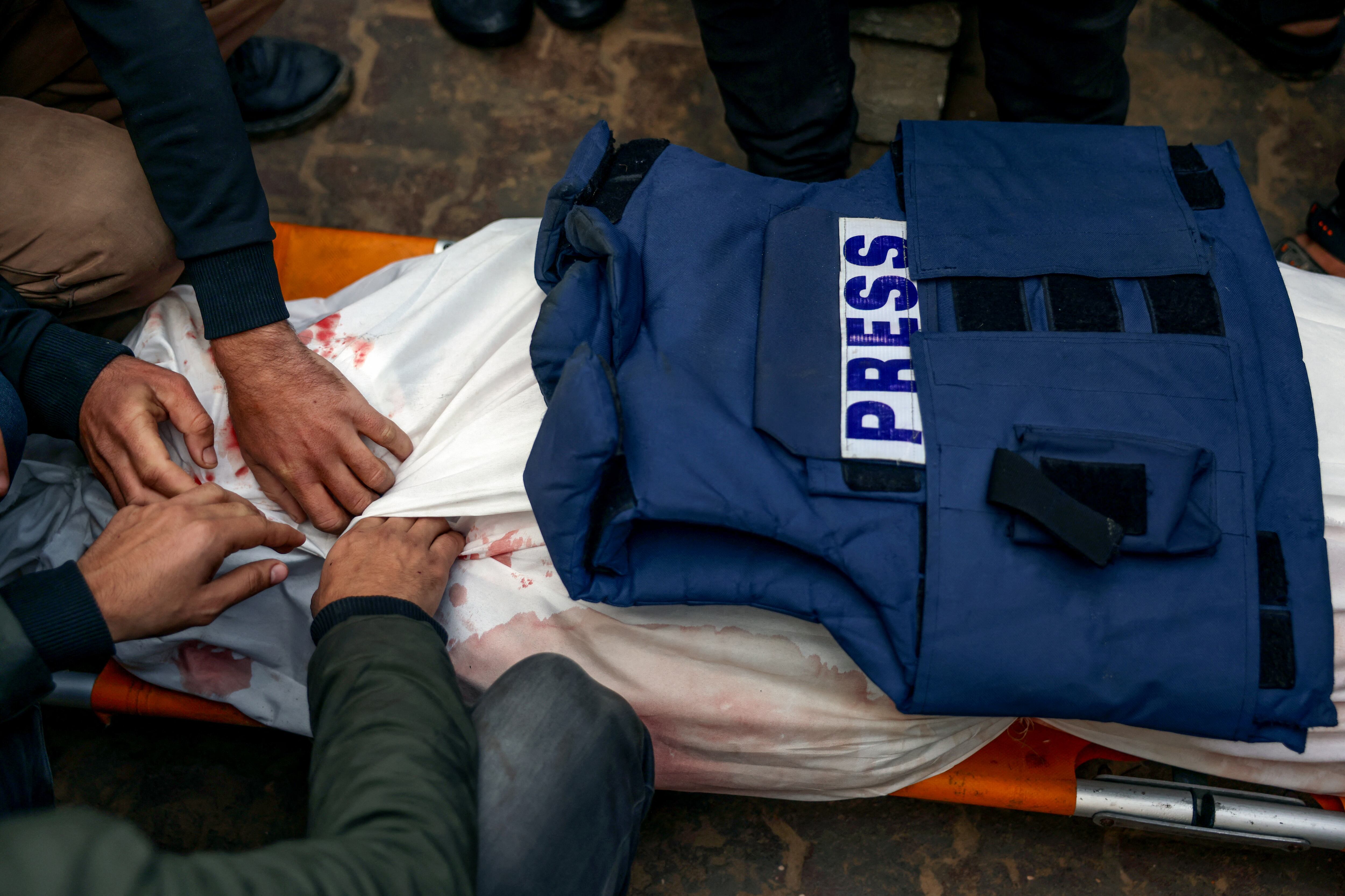 Los dolientes se preparan para enterrar el cuerpo del periodista palestino Ahmed Al-Shayah, cubierto con un chaleco de prensa, después de que fuera asesinado durante un ataque israelí la noche anterior en Khan Yunis, en el Hospital Nasser, en el sur de la Franja de Gaza. (Foto de BASHAR TALEB / AFP)
