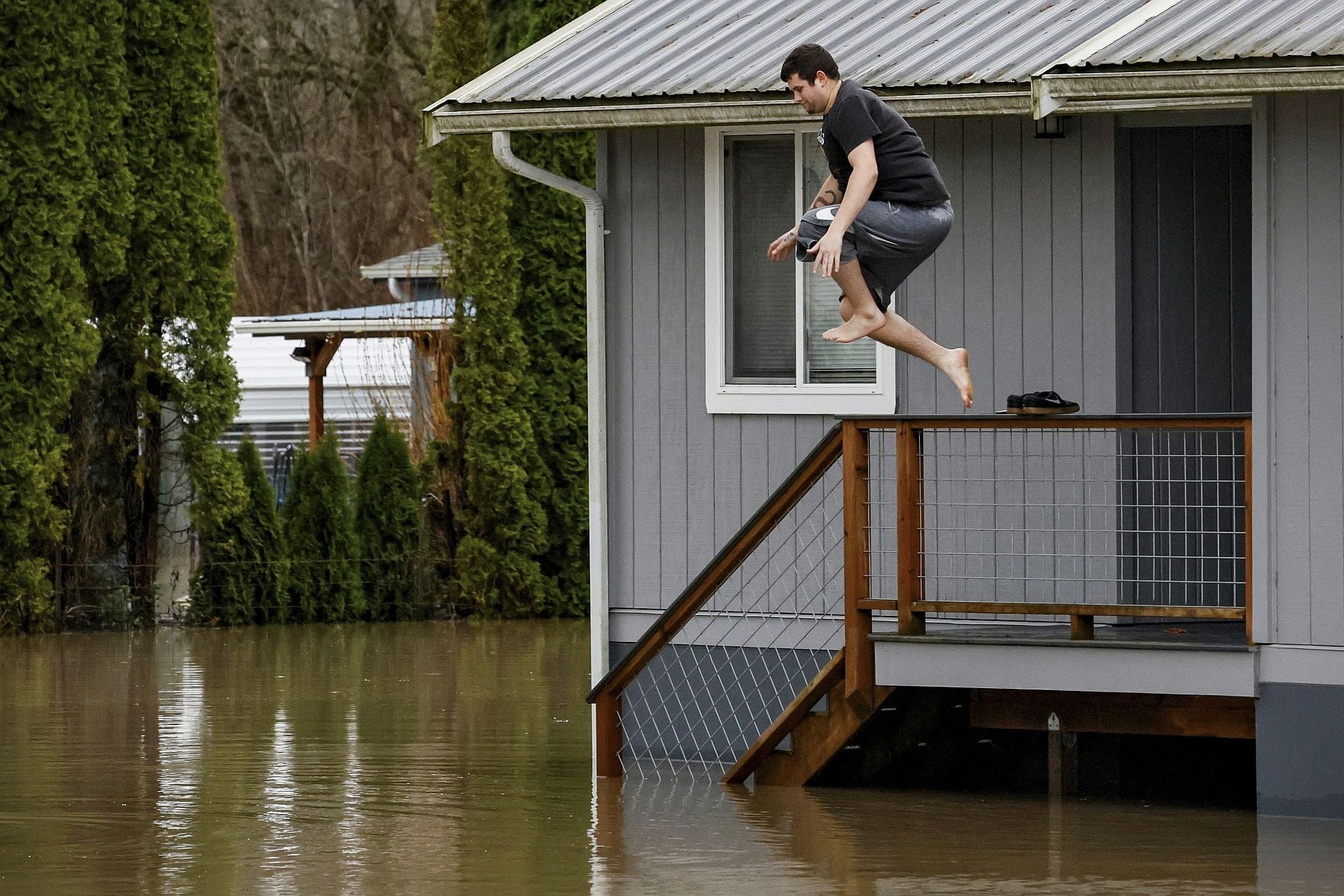 Bryce Humerickhouse salta desde la terraza de su casa alquilada a las aguas de la inundación que la rodean en Hamilton, Washington, después de sacar algunos objetos de valor el jueves 11 de diciembre de 2025. (Jennifer Buchanan/The Seattle Times vía AP)
