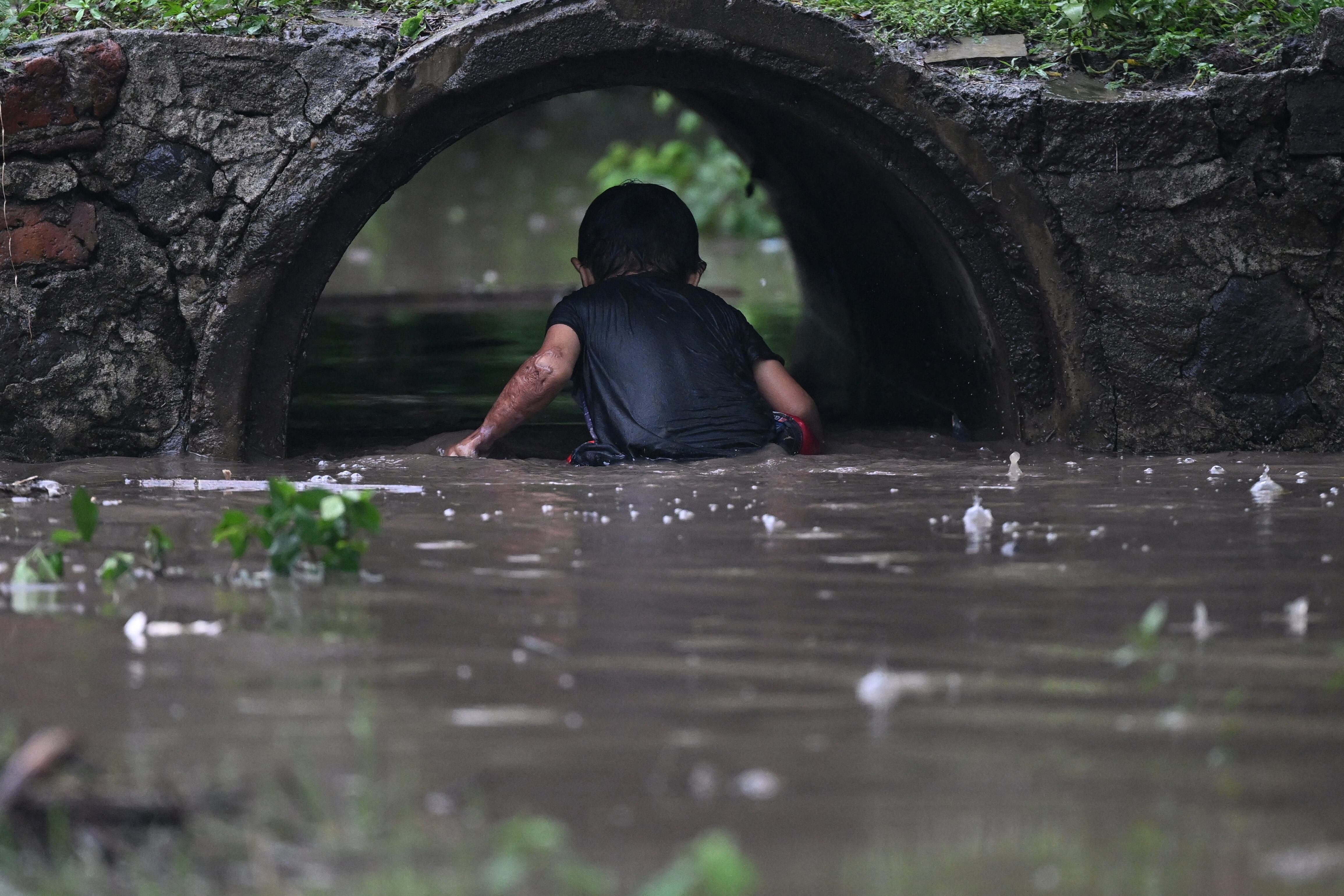 Un niño juega en el agua durante la alerta roja decretada por el gobierno de El Salvador debido a la tormenta tropical Pilar. (Foto de Marvin RECINOS / AFP).