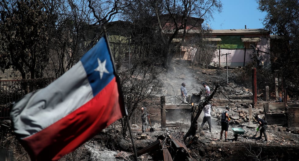 Una bandera de Chile ondea mientras los vecinos inspeccionan casas quemadas en Villa Independencia, región de Valparaíso, el 5 de febrero de 2024. (Foto de Javier TORRES/AFP).