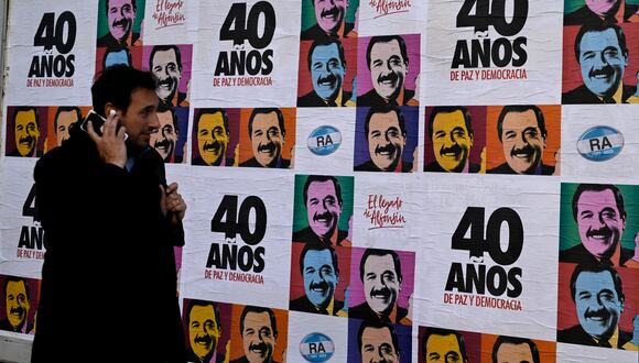 Un hombre camina junto a pancartas alusivas a la celebración del 40 aniversario del retorno de la democracia en Argentina y la elección del fallecido expresidente (1983-1989) Raúl Alfonsín. (Foto de LUIS ROBAYO / AFP).