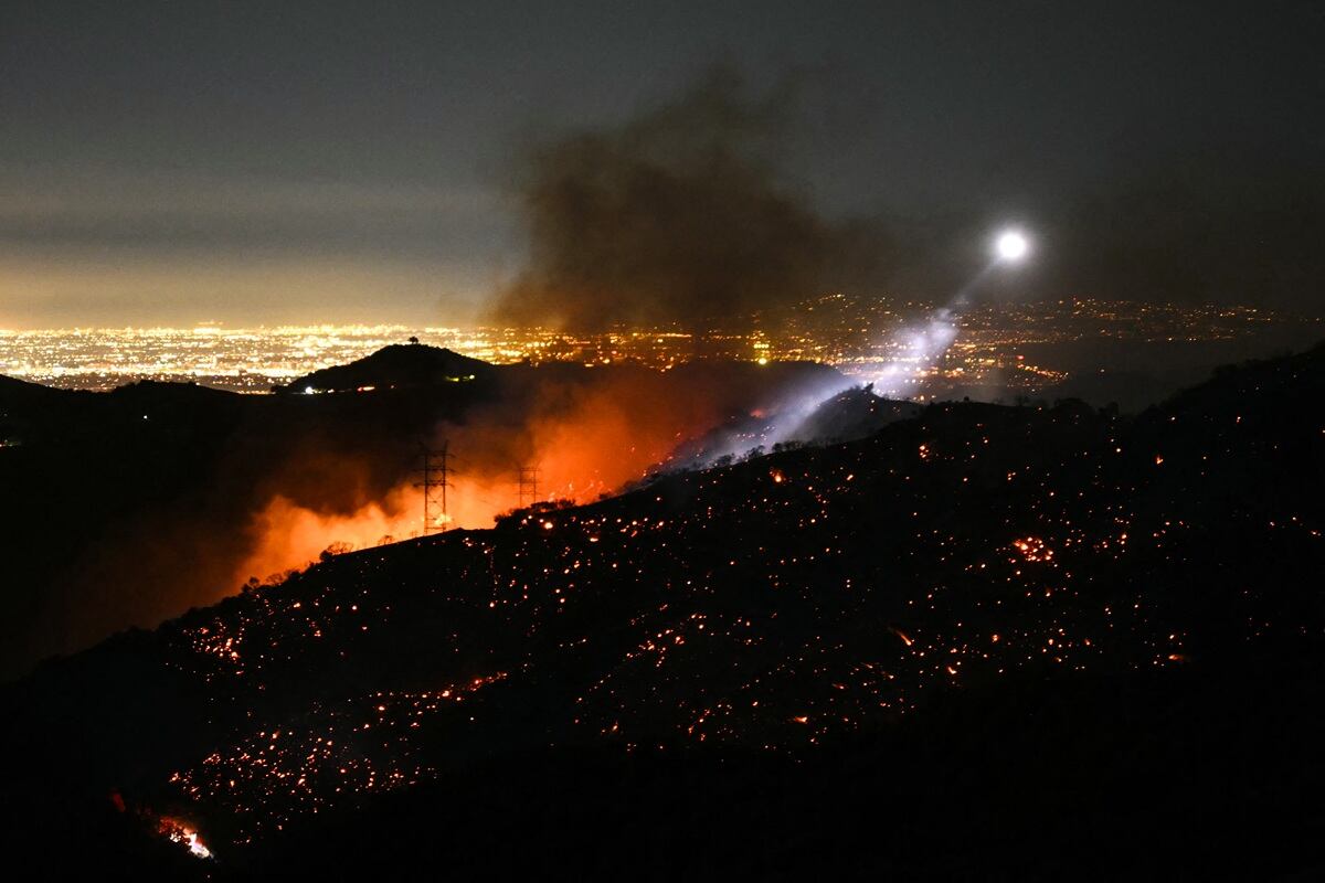 La luz de un helicóptero contra incendios ilumina una ladera humeante mientras el incendio de Palisades crece cerca del vecindario de Mandeville Canyon y Encino, California, el 11 de enero de 2025. (Foto de Patrick T. Fallon / AFP)