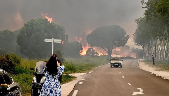 Una mujer toma una fotografía de un incendio forestal que provocó la evacuación de más de 3.000 personas de campamentos cercanos en Saint-Andre, cerca de Argeles-sur-Mer, en el suroeste de Francia, el 14 de agosto de 2023. (Foto de Raymond ROIG / AFP)