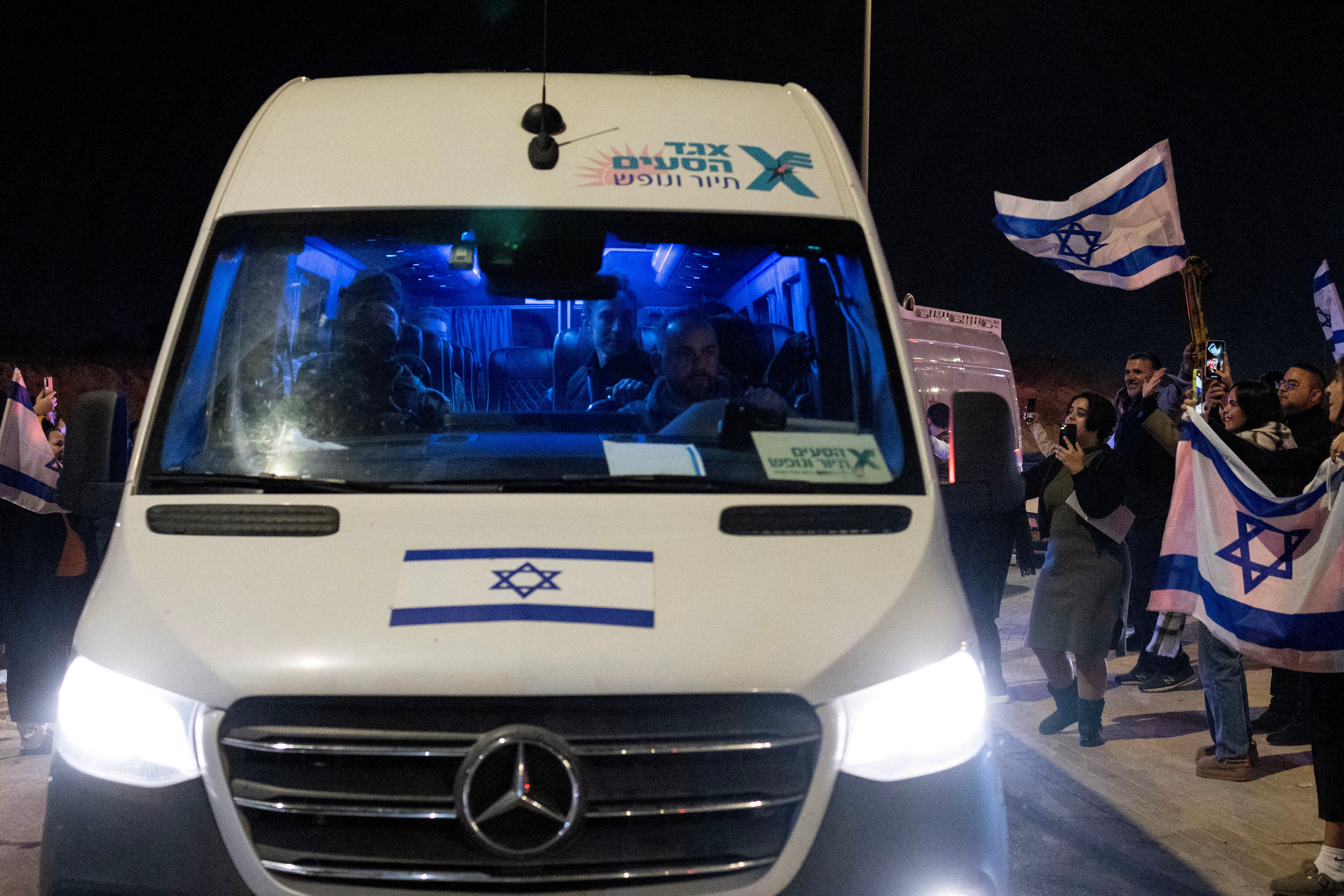 Ciudadanos sostienen banderas israelíes mientras los rehenes liberados llegan en un vehículo a las afueras de la base militar de Ofakim, en el sur de Israel, el 1 de diciembre de 2023. (Foto de Oren ZIV / AFP).