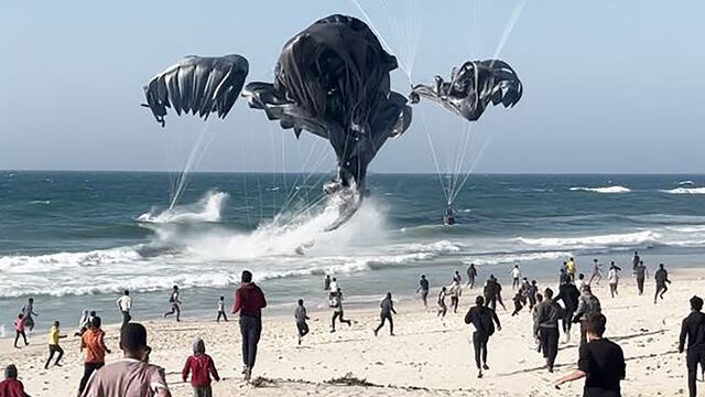 Palestinos corren hacia paracaídas que sujetan paquetes de alimentos lanzados desde aviones estadounidenses en una playa en la Franja de Gaza el 2 de marzo de 2024. (Foto de AFP).