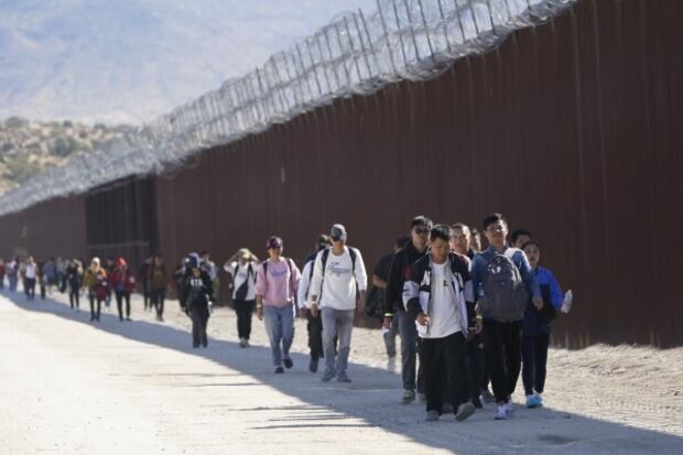 Un grupo de personas, entre ellas muchas de China, camina a lo largo del muro después de cruzar la frontera con México el 24 de octubre del 2023. (Foto: AP / Gregory Bull).