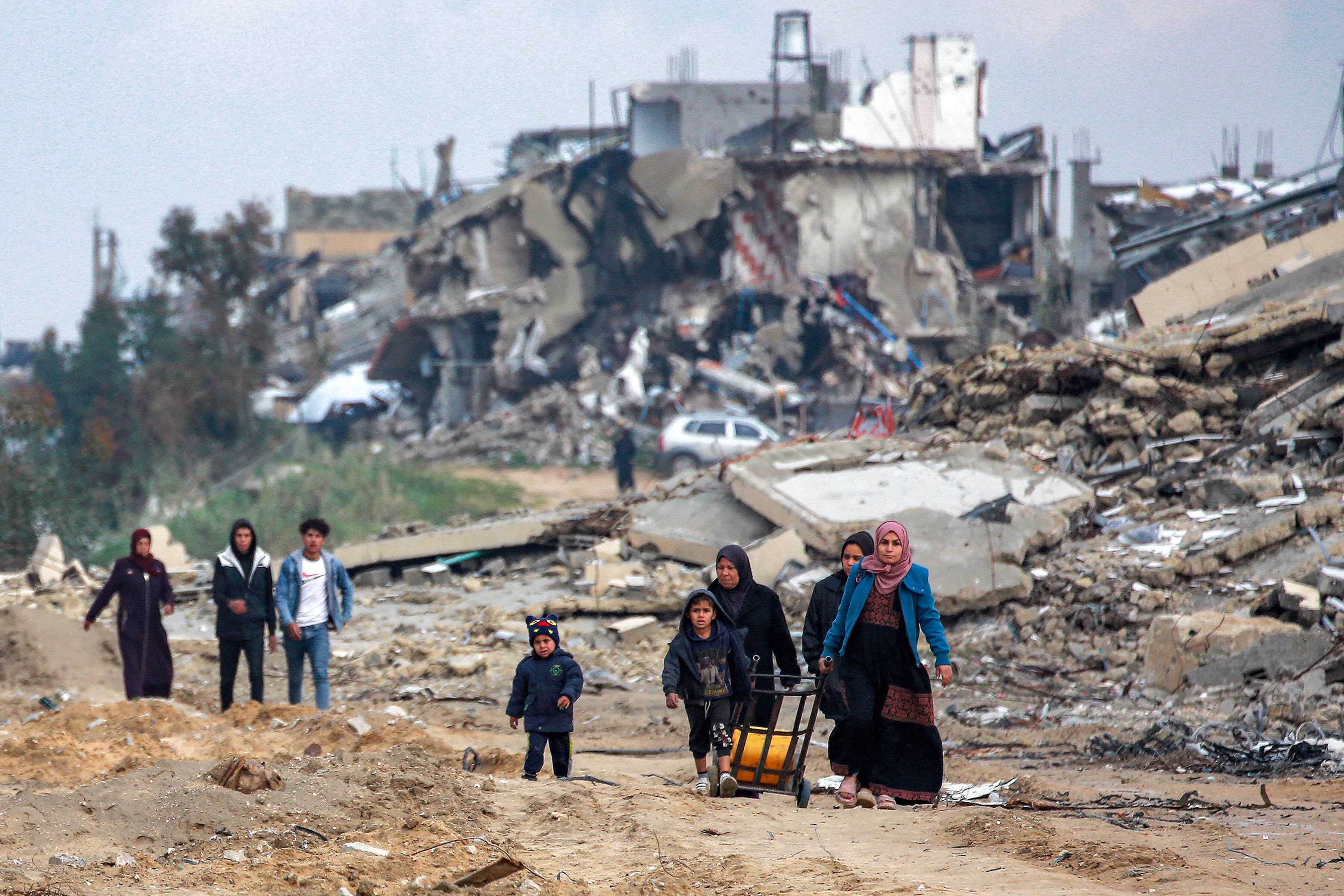 Mujeres y niños caminan por una carretera destruida, pasando por edificios derrumbados en el oeste de Beit Lahia, en el norte de la Franja de Gaza. (Foto de BASHAR TALEB / AFP)