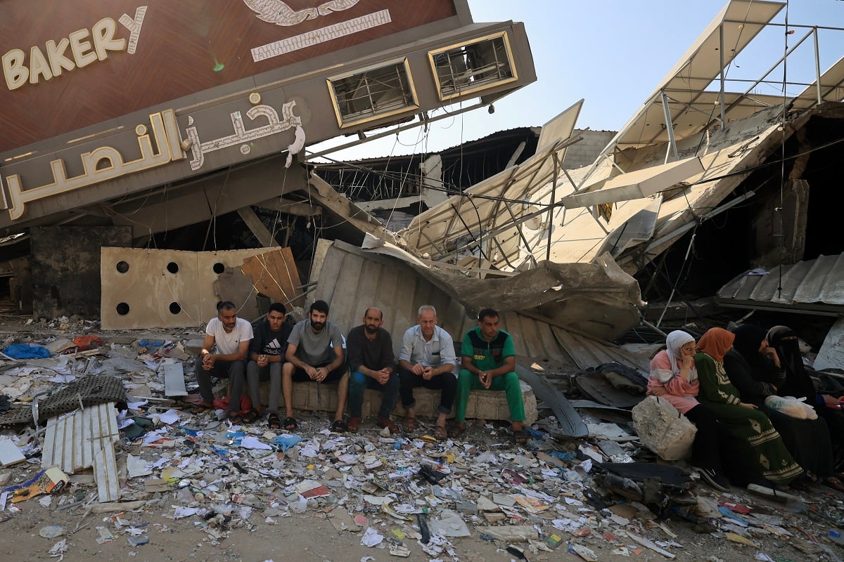 Gente se sienta frente a una panadería que fue parcialmente destruida en un ataque israelí, en el campo de refugiados de Nuseirat en el centro de la Franja de Gaza, el 2 de noviembre de 2023. (Foto de Mahmud HAMS / AFP)