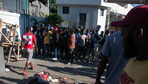 La gente mira el cuerpo de un hombre que estaba entre una docena asesinado en la calle por pandilleros, en Pétionville, Puerto Príncipe, Haití, el 18 de marzo de 2024. (Foto de Clarens SIFFROY / AFP)