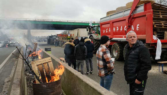 Manifestantes se encuentran junto a un barril de fuego y tractores que bloquean la autopista A15 cerca de Argenteuil, al noroeste de París, el 30 de enero de 2024. (Foto de Dimitar DILKOFF / AFP)