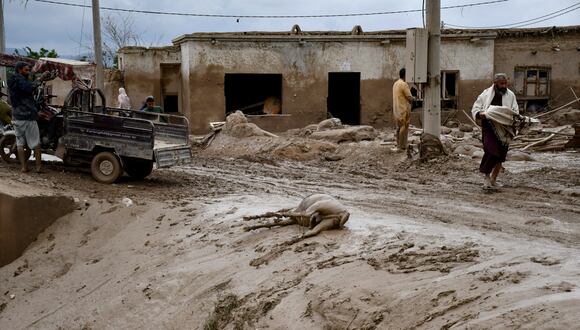 Hombres afganos pasan junto al cadáver de un burro a lo largo de una calle cubierta de barro después de inundaciones repentinas tras fuertes lluvias en una aldea en el distrito de Baghlan-e-Markazi de la provincia de Baghlan el 11 de mayo de 2024. (Foto de Atif Aryan / AFP)