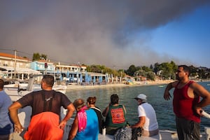 Personas son evacuadas en pequeñas embarcaciones durante un incendio forestal mientras una columna de humo se eleva hacia el cielo cerca del pueblo de Siviri, en el norte de Grecia, el 13 de agosto de 2026. (Vasilis VERVERIDIS / AFP)