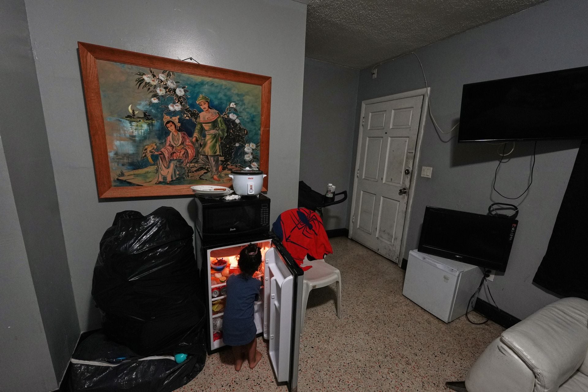 El hijo de dos años de Yaoska, una solicitante de asilo embarazada, busca un snack en el pequeño refrigerador de la habitación de motel donde viven en la zona de Miami, luego de que su padre fue deportado a Nicaragua, el 13 de noviembre de 2025. (AP Foto/Rebecca Blackwell)
