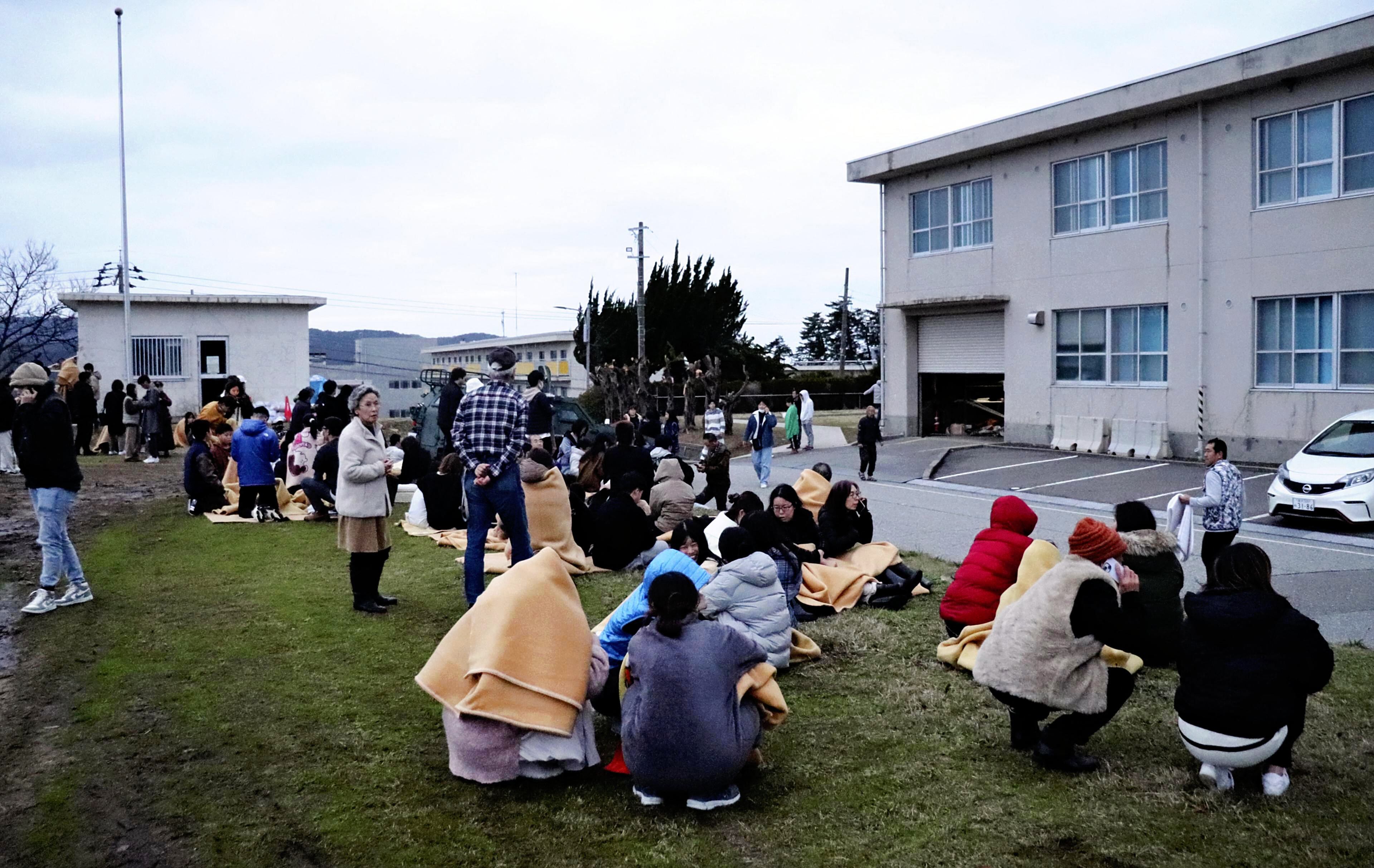 La gente se sienta al aire libre después de ser evacuada de los edificios en la ciudad de Wajima, prefectura de Ishikawa, el 1 de enero de 2024, después de que un gran terremoto sacudiera Japón. (Foto de Yusuke FUKUHARA / Yomiuri Shimbun / AFP).