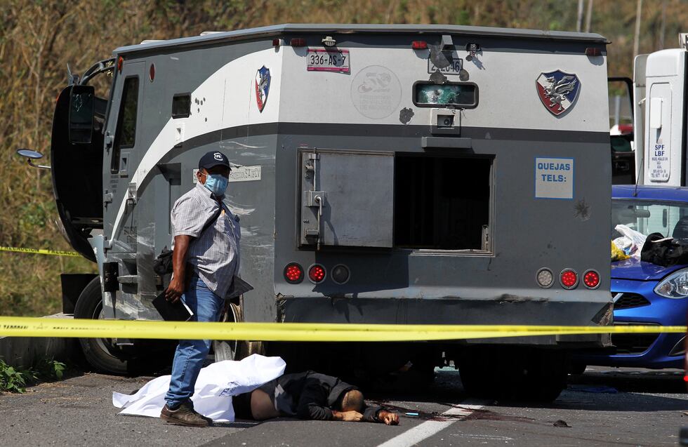 Un hombre junto a un cadáver luego de que un camión de transporte de seguridad fuera emboscado por un grupo armado que mató a cuatro guardias privados en un asalto en la carretera Guadalajara-El Arenal. (Foto de ULISES RUIZ / AFP).