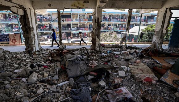 Los niños pasan junto a un aula destruida donde se refugiaban personas en una escuela administrada por la Agencia de Obras Públicas y Socorro de las Naciones Unidas para los Refugiados de Palestina (OOPS) que anteriormente fue atacada por bombardeos israelíes. (Foto de Eyad BABA / AFP)