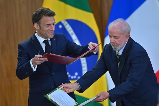 El presidente de Brasil Luiz Inácio Lula da Silva (der) y su homólogo de Francia Emmanuel Macron firman unos acuerdos bilaterales este jueves en Brasilia. (EFE/Andre Borges).