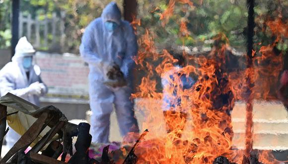 Imagen referencial. Los familiares y parientes que usan equipo de protección se paran junto a la pira funeraria de una víctima del coronavirus en un crematorio en Nueva Delhi, India, el 24 de mayo de 2021. (Sajjad HUSSAIN / AFP).