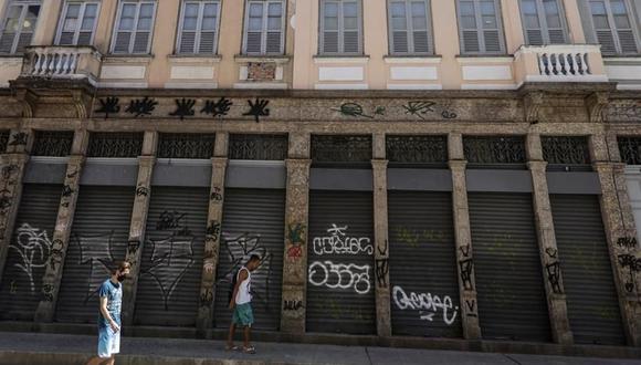 Dos hombres caminan frente a locales comerciales cerrados en Río de Janeiro, Brasil, debido a la pandemia de coronavirus. (EFE/ Antonio Lacerda).