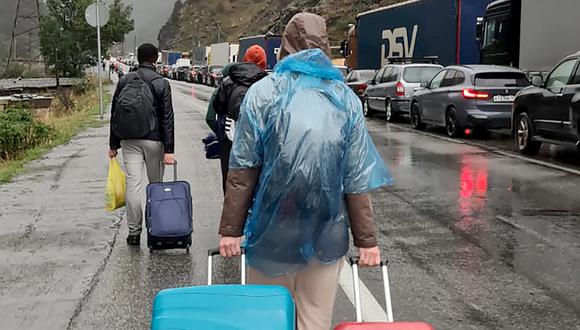 Las personas que transportan equipaje pasan junto a vehículos con matrículas rusas en el lado ruso de la frontera hacia el puesto de control aduanero de Nizhniy Lars entre Georgia y Rusia, a unos 25 km de la ciudad de Vladikavkaz, el 25 de septiembre de 2022.  (Foto por AFP)