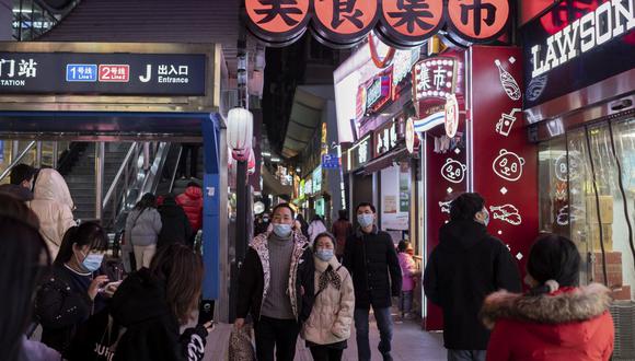 Imagen referencial. Personas con mascarillas caminan por una calle de Wuhan el 10 de enero de 2021. (NICOLAS ASFOURI / AFP).