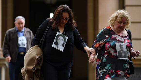 Miembros de una comunidad australiana chilena sostienen fotos de algunas víctimas luego de una comparecencia de Adriana Rivas este martes, en Sídney. (Foto: EFE)