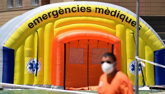 Un hombre con una máscara facial pasa frente a un hospital de campaña establecido para casos de coronavirus en las afueras del Hospital Universitario Arnau de Vilanova, en Lleida, Cataluña, España. (Foto por Pau BARRENA / AFP).