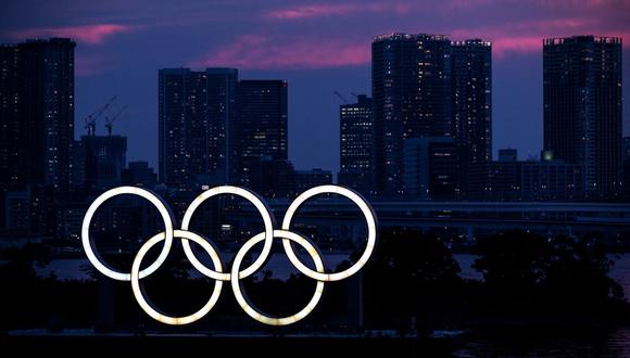 Una vista general muestra los anillos olímpicos iluminados al anochecer en el paseo marítimo de Odaiba en Tokio, Japón, el 12 de Julio de 2021. (Charly TRIBALLEAU / AFP).