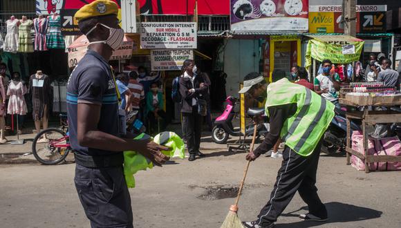 Un oficial de policía supervisa a un ciudadano de chaleco amarillo mientras barre las calles tras ser intevenido por no usar mascarilla en el centro de Antananarivo, capital de Madagascar. (Foto: AFP)