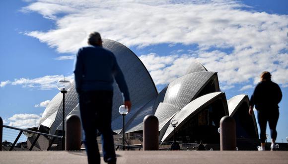 Esta imagen tomada el 26 de junio de 2021 muestra a personas caminando frente a la Ópera de Sídney durante el cierre por coronavirus en esa ciudad de Australia. (Foto de Saeed KHAN / AFP).
