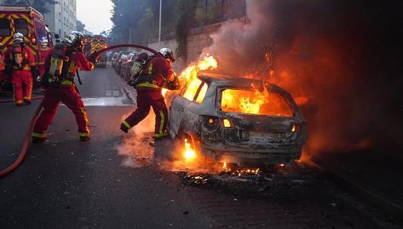 Bomberos trabajan para apagar un automóvil en llamas al margen de una manifestación en Nanterre, al oeste de París, el 27 de junio de 2023, luego de que la policía francesa matara a un adolescente. (Foto de Zakaria ABDELKAFI / AFP)