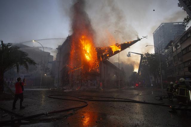 La cúpula de la iglesia de La Asunción cae ardiendo en llamas después de ser incendiada por manifestantes en la conmemoración del primer aniversario del levantamiento social en Chile. (Foto de CLAUDIO REYES / AFP).
