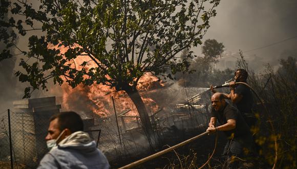 Los hombres rocían agua sobre un incendio forestal en Chasia, en las afueras de Atenas, el 22 de agosto de 2023. (Foto de Angelos Tzortzinis / AFP)