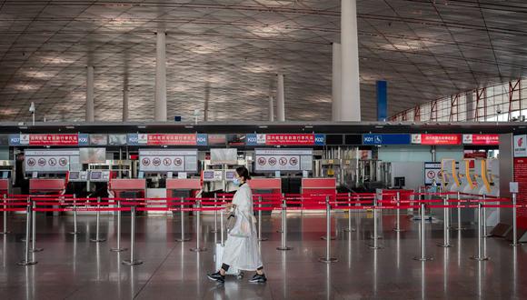 Imagen referencial. Un pasajero con una máscara facial por el coronavirus camina en una terminal casi vacía en el Aeropuerto Internacional de Beijing, China, el 13 de abril de 2020. (NICOLAS ASFOURI / AFP).