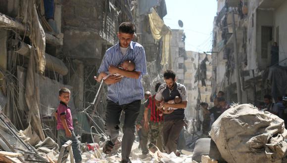 Hombres sirios que cargan bebés se abren paso a través de los escombros de los edificios destruidos luego de un ataque aéreo en el vecindario de Salihin, el 11 de septiembre de 2016. (Foto de Ameer al-HALBI / AFP).