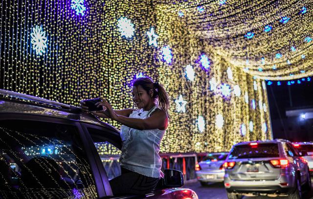 Una mujer sale por la ventana del auto para tomarse un selfie con las luces de Navidad colocadas en el puente sobre el río Guaire en Caracas, Venezuela. (AFP / Yuri CORTEZ).