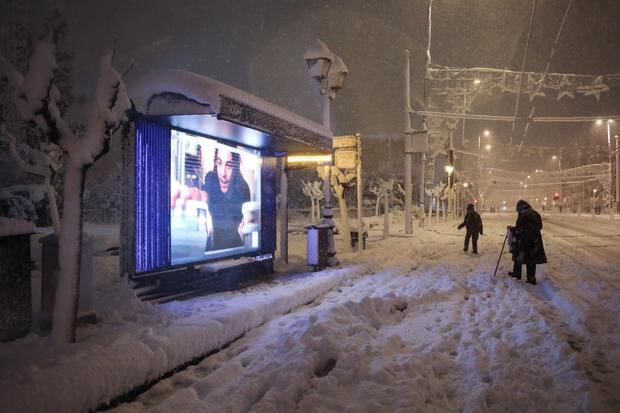 People walk past a bus stop during a heavy snowfall in central Athens, Greece.  (EFE/EPA/GEORGE VITSARAS).
