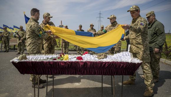 Varios soldados colocan una bandera ucraniana sobre el cadáver de su compañero de armas Mykola durante su entierro en el cementerio militar de Dnipro (Ucrania) el 4 de mayo de 2022. EFE/Miguel Gutiérrez