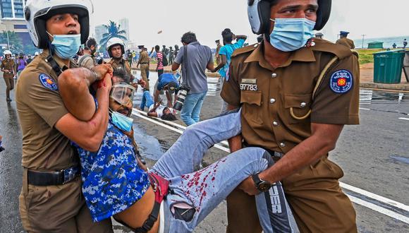 Policías cargan a un hombre herido durante un enfrentamiento entre partidarios del gobierno y manifestantes frente a la oficina del presidente de Sri Lanka en Colombo el 9 de mayo de 2022. (Ishara S. KODIKARA / AFP).
