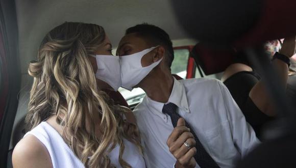 Con mascarillas para prevenir contagios de COVID-19, Thiago do Nascimento, derecha, y Keilla de Almeida se besan en un automóvil durante su boda en la oficina del registro civil, en el vecindario de Santa Cruz, Río de Janeiro, Brasil. (Foto: AP/Silvia Izquierdo)