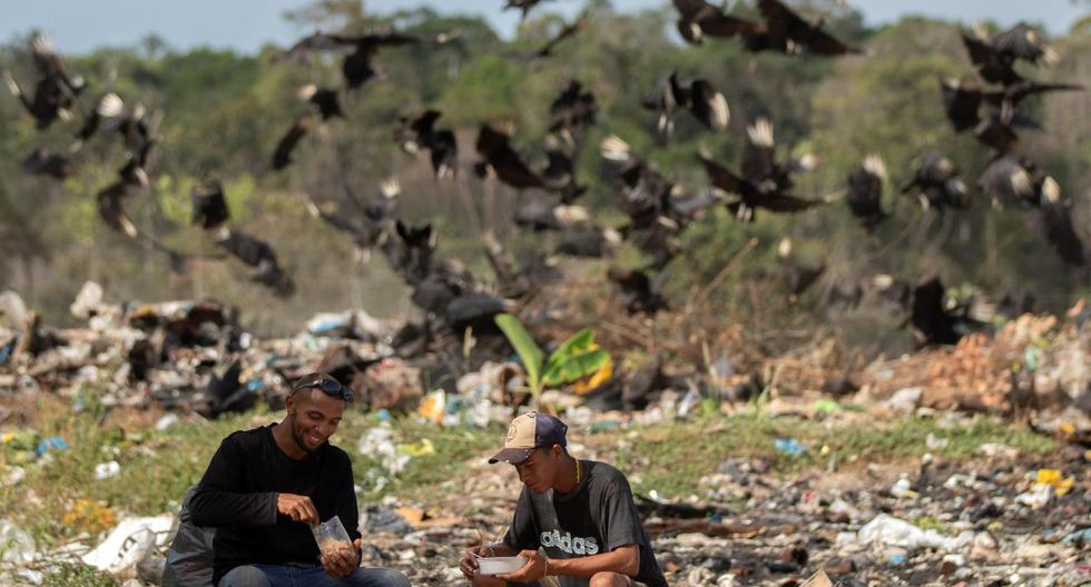 Venezolanos son vistos comiendo en el basurero municipal de Pacaraima. En el fondo una bandada de buitres los acechan. (EFE)