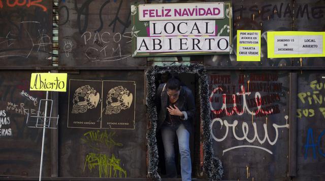 Una mujer sale de una tienda amurallada con un letrero que dice "Feliz Navidad", debido a las violentas protestas en Valparaíso, muchos han forrado las con tapas gruesas de metal sus negocios. (Foto: AFP).