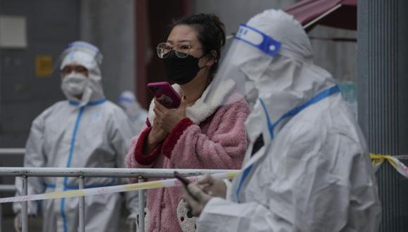 Una mujer se interpone entre los trabajadores con trajes protectores mientras espera sus compras en un vecindario cerrado como parte de los controles de COVID-19 en Beijing.